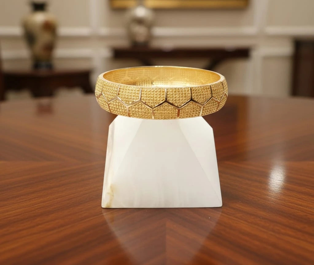 Gold bracelet on a white stand on a wooden surface