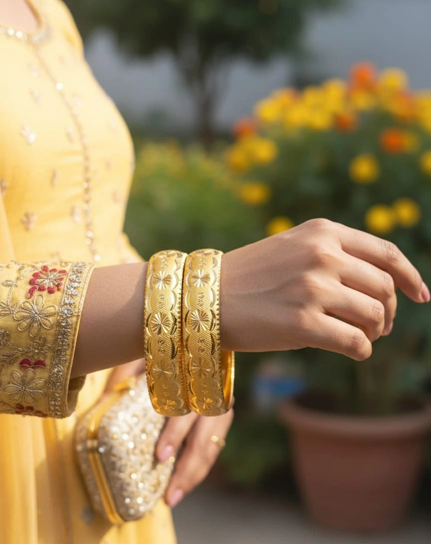 Person wearing gold bangles with a blurred background of flowers and greenery