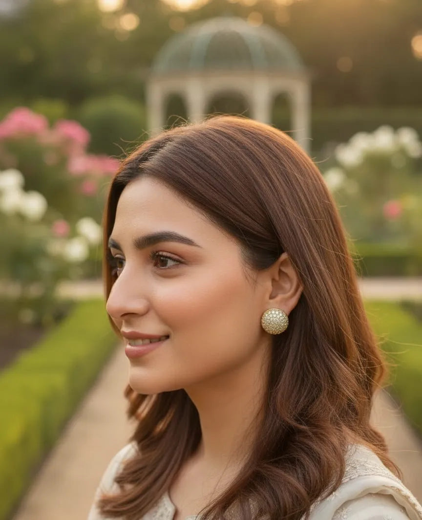 Woman with long brown hair and earrings standing in a garden with a gazebo in the background