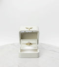 Gold ring in an open white jewelry box on a light gray background
