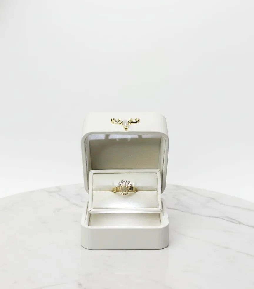 Gold ring in an open white jewelry box on a light gray background