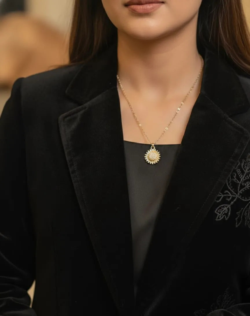 Person wearing a black blazer with a gold necklace featuring a sun pendant.