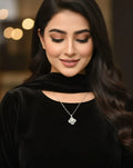 Woman wearing a black outfit with a necklace featuring a rose pendant, set against a blurred background.