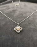 Silver necklace with a floral pendant featuring a pearl on a gray surface