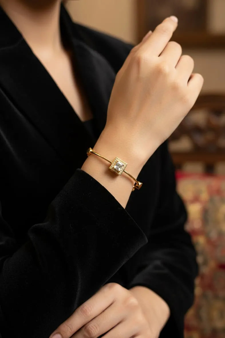 Gold bracelet with a diamond on a person's wrist, wearing a black outfit.