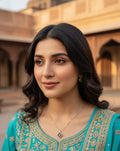 Woman in a teal traditional outfit with intricate patterns, standing in front of architectural background.
