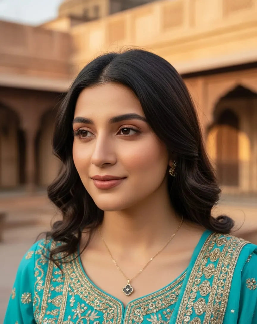 Woman in a teal traditional outfit with intricate patterns, standing in front of architectural background.