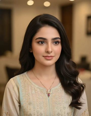 Woman with long, wavy hair wearing a beige embroidered top indoors.