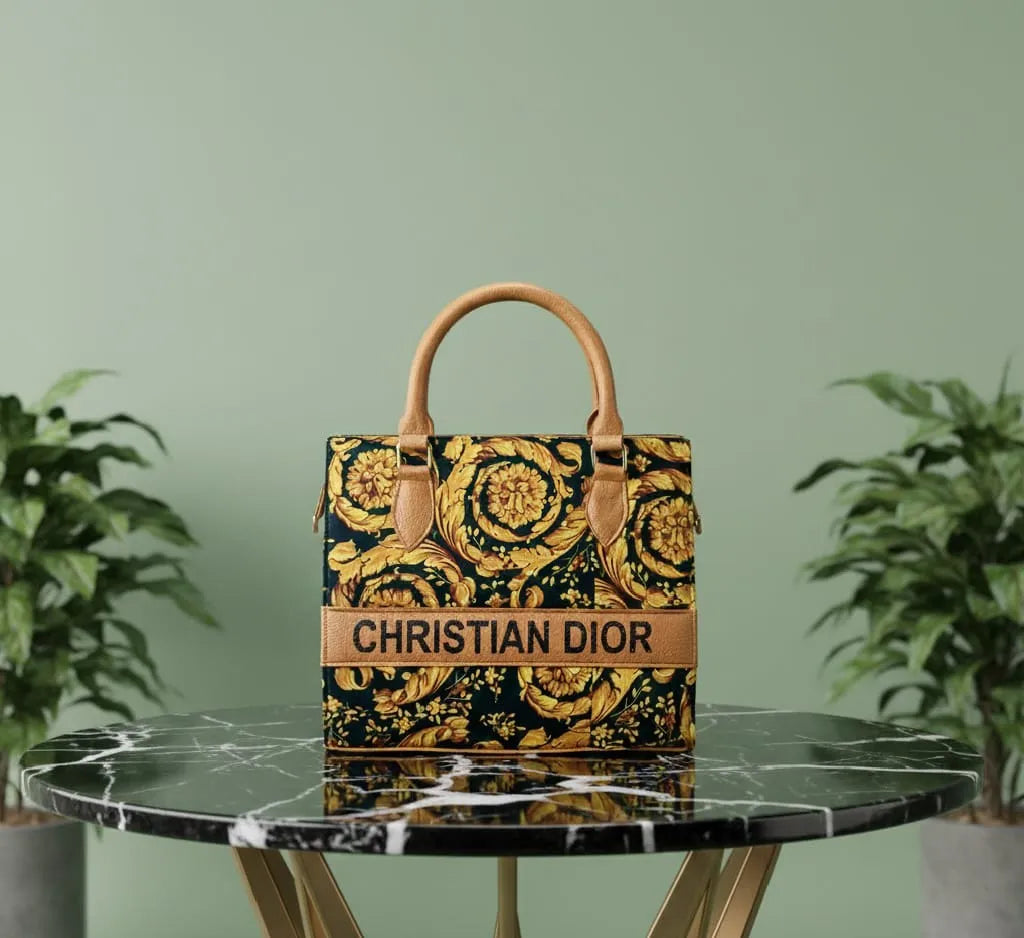 Christian Dior handbag with gold and black design on a marble table with green plants.