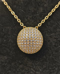 Gold necklace with a round, diamond-studded pendant on a black background