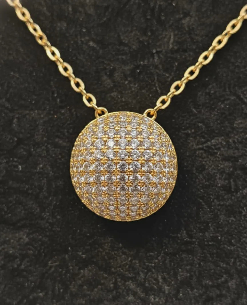Gold necklace with a round, diamond-studded pendant on a black background