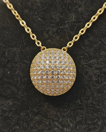 Gold necklace with a round, diamond-studded pendant on a black background