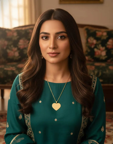Woman wearing a green traditional outfit with a gold necklace in an indoor setting.