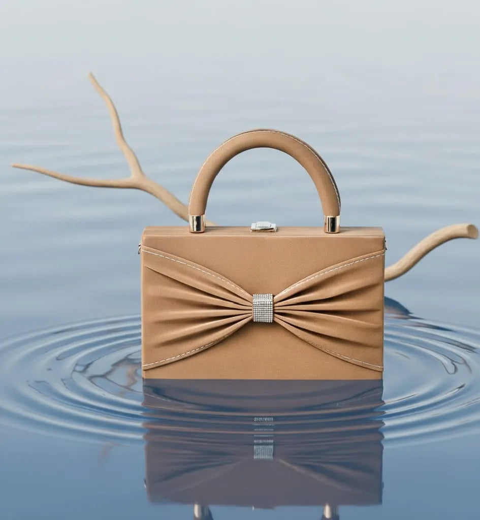 Tan handbag with a decorative bow on a reflective water surface