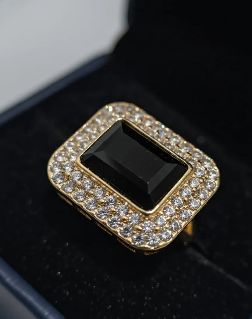 Hand wearing a silver ring with a black gemstone against a floral-patterned wall.