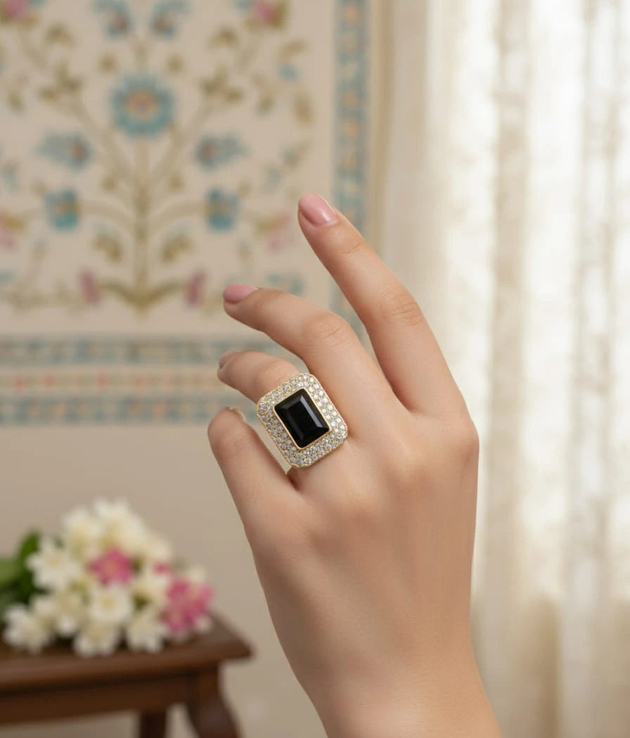 Hand wearing a silver ring with a black gemstone against a floral-patterned wall.