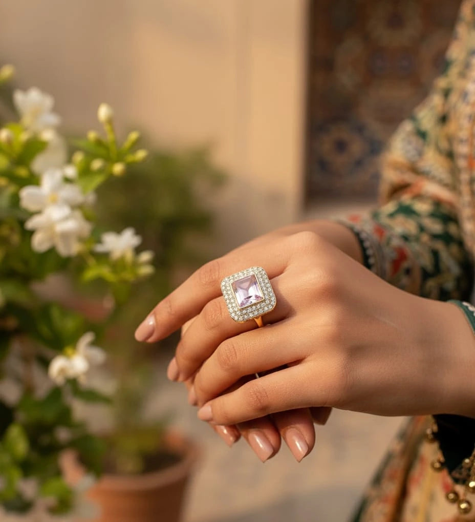 Hand wearing a ring with a pink gemstone, blurred floral background