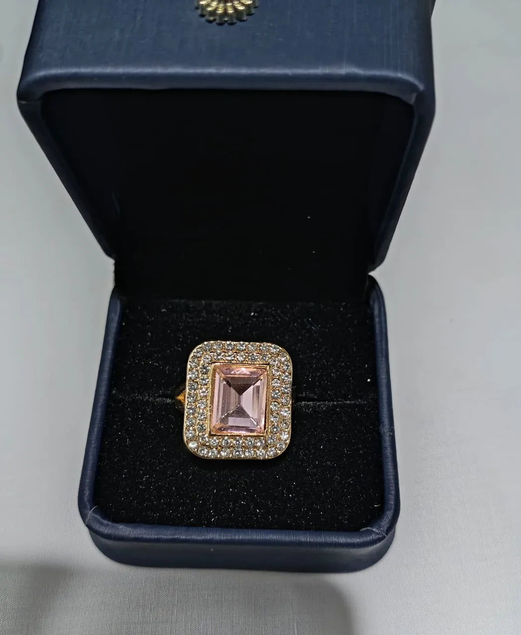 Hand wearing a ring with a pink gemstone, blurred floral background