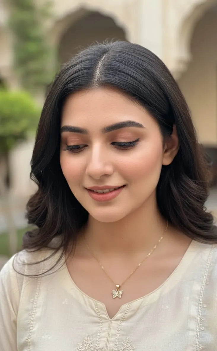 Woman with dark hair and a light-colored top, wearing a butterfly necklace, outdoors.