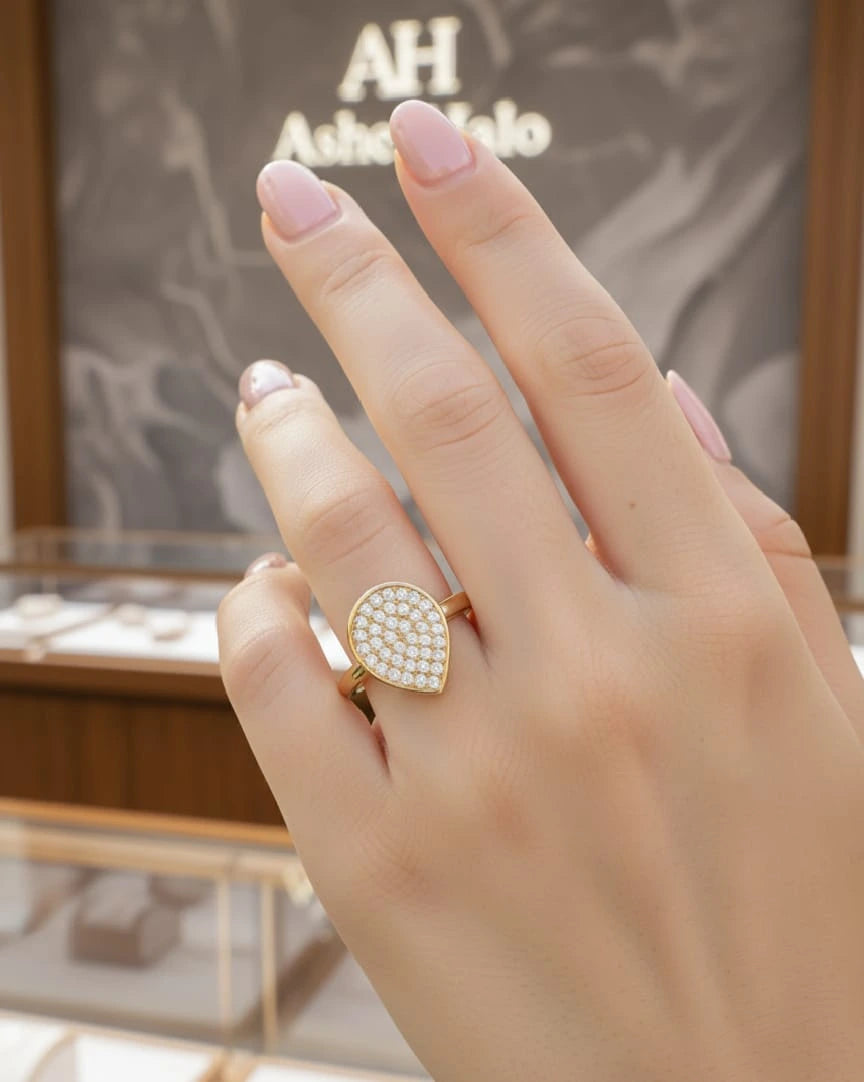 Hand wearing a gold ring with a diamond-like center, set against a blurred jewelry store background.