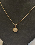 Gold necklace with a round, diamond-studded pendant on a black stand.