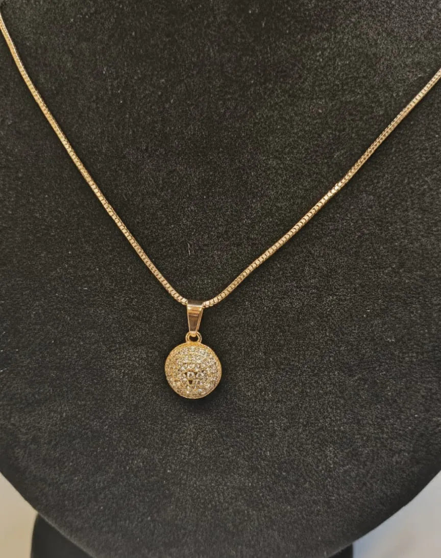 Gold necklace with a round, diamond-studded pendant on a black stand.