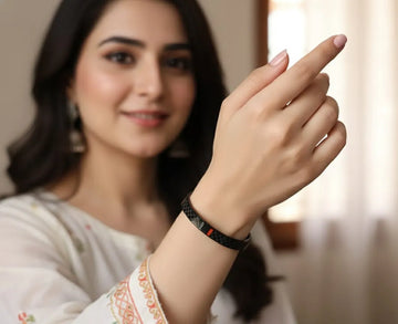 Woman wearing a black wristband, smiling and pointing at it.
