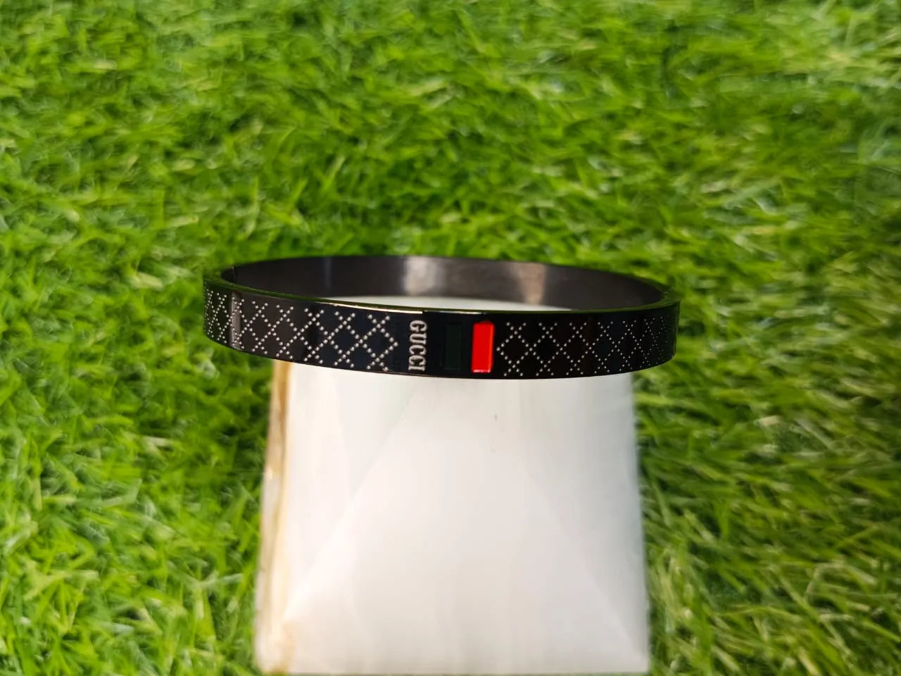 Black bracelet with a red tag on a white cylindrical object against a green grass background