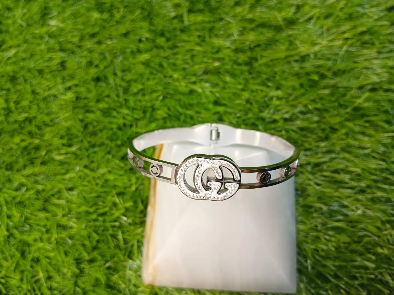 Silver ring with a prominent logo on a white stand against a grassy background
