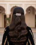 Person with long, wavy hair wearing a decorative hair clip, standing in front of an architectural background.