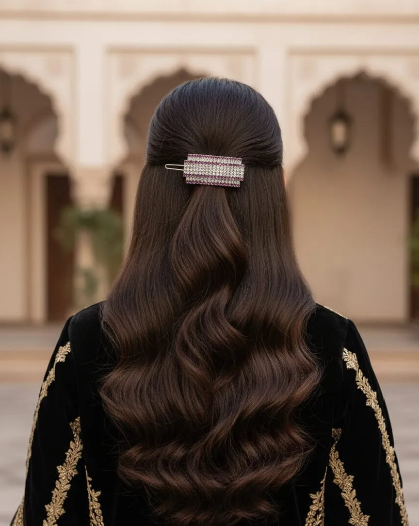 Person with long, wavy hair wearing a decorative hair clip, standing in front of an architectural background.