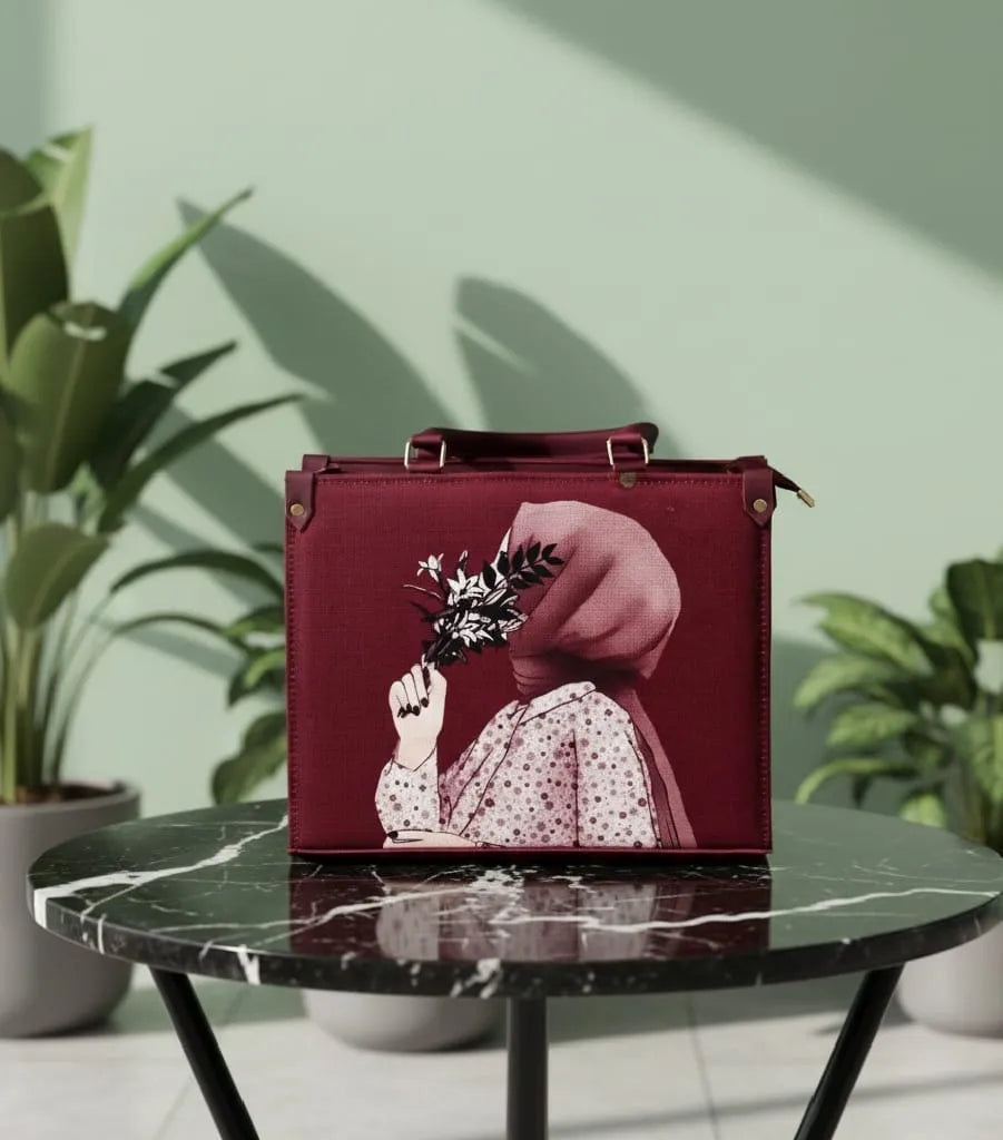 Maroon handbag with artistic design on a marble table against a light green wall with plants.