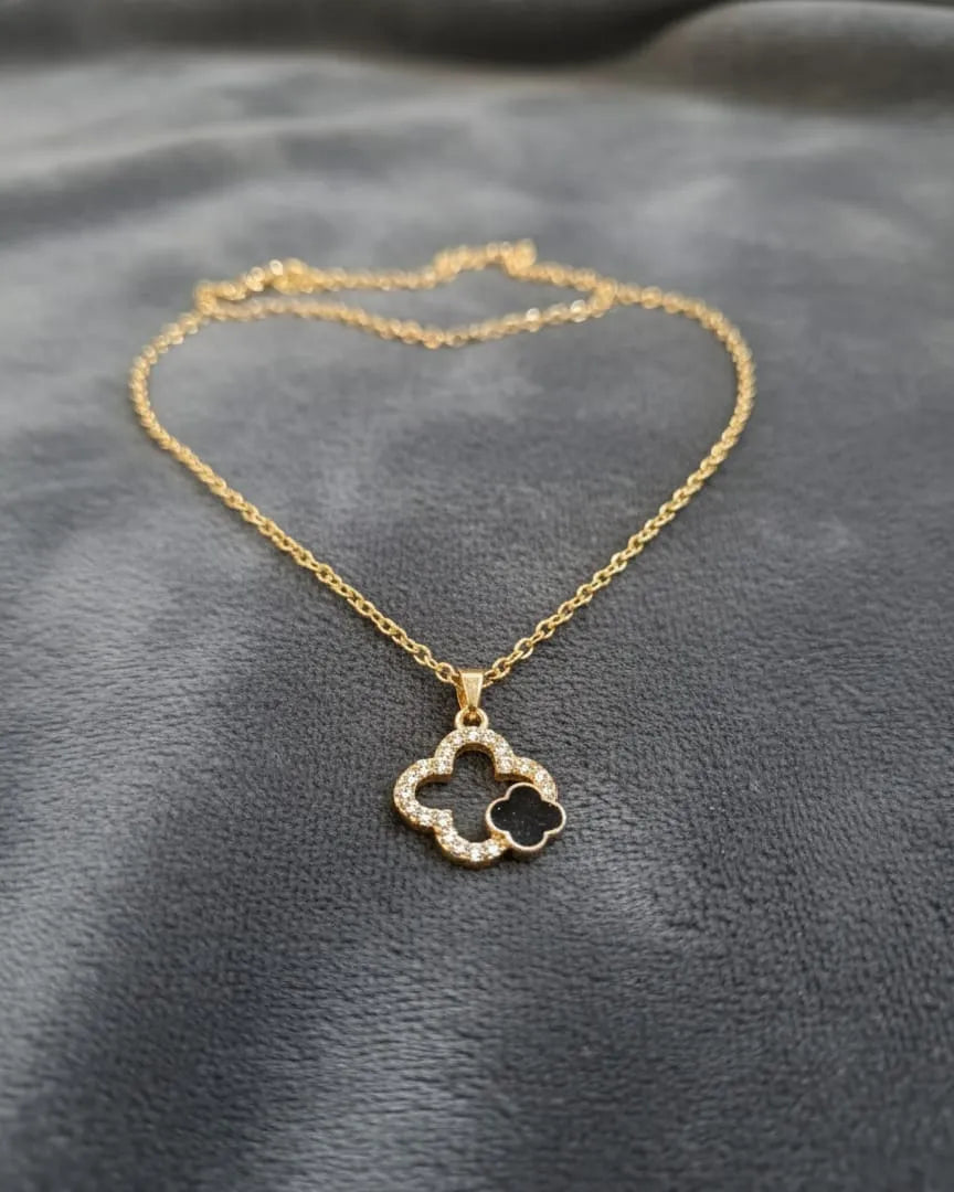 Gold necklace with a clover-shaped pendant on a gray fabric background