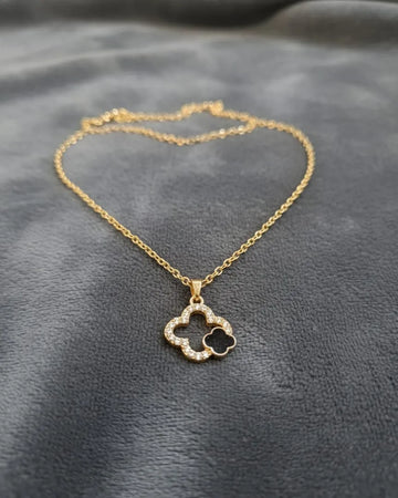 Gold necklace with a clover-shaped pendant on a gray fabric background