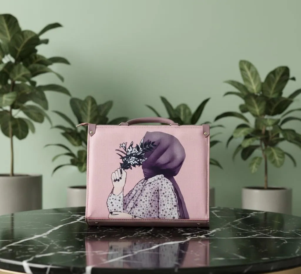 Pink handbag with artistic design on a marble surface with plants in the background