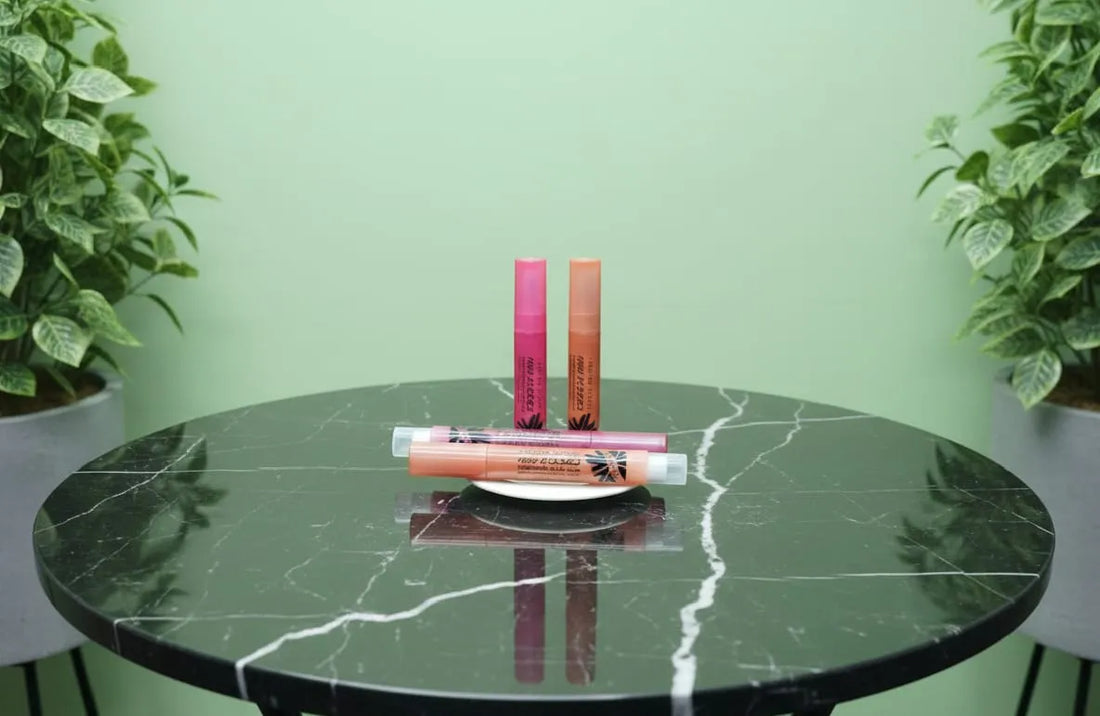 Lip glosses on a round marble table with a green background and plants.