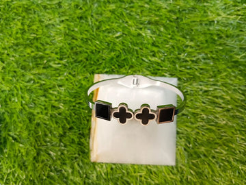 Bracelet with black and gold designs on a white card, placed on grass