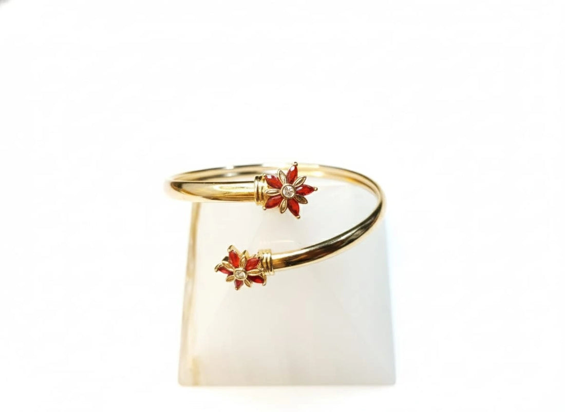 Gold bracelet with red floral accents on a white background