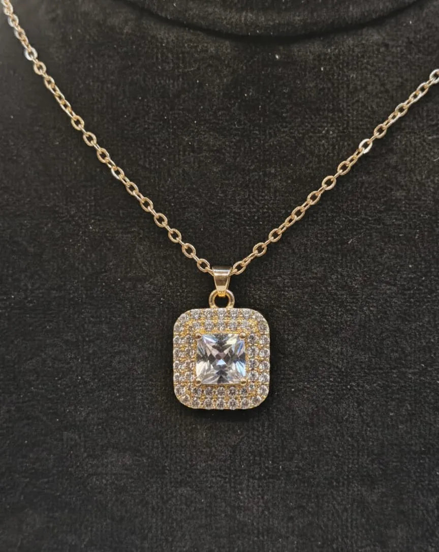 Gold necklace with a square pendant featuring a central diamond on a black background