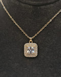 Gold necklace with a square pendant featuring a central diamond on a black background