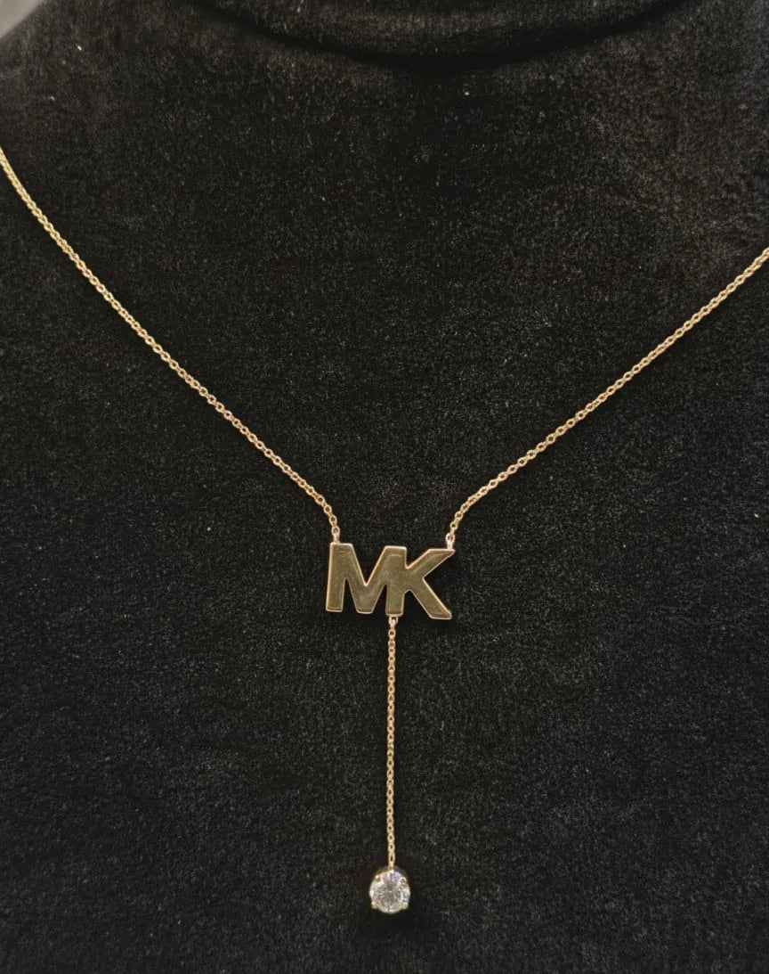Woman wearing a necklace with a 'MK' pendant indoors