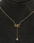Gold necklace with 'MK' pendant on a black background