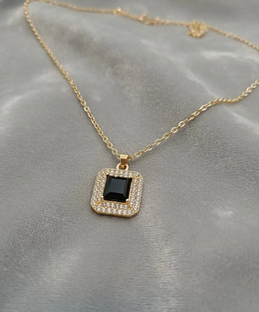 Gold necklace with a black square pendant on a gray fabric background