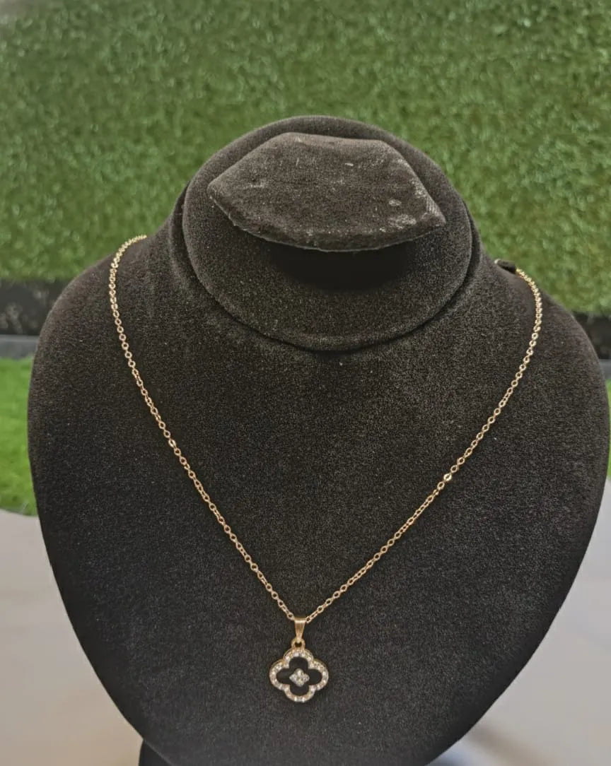 Gold necklace with a pendant on a black velvet stand against a green textured background