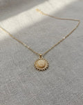 Gold necklace with a sunflower pendant on a light gray fabric background