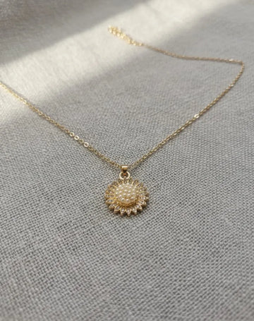 Gold necklace with a sunflower pendant on a light gray fabric background
