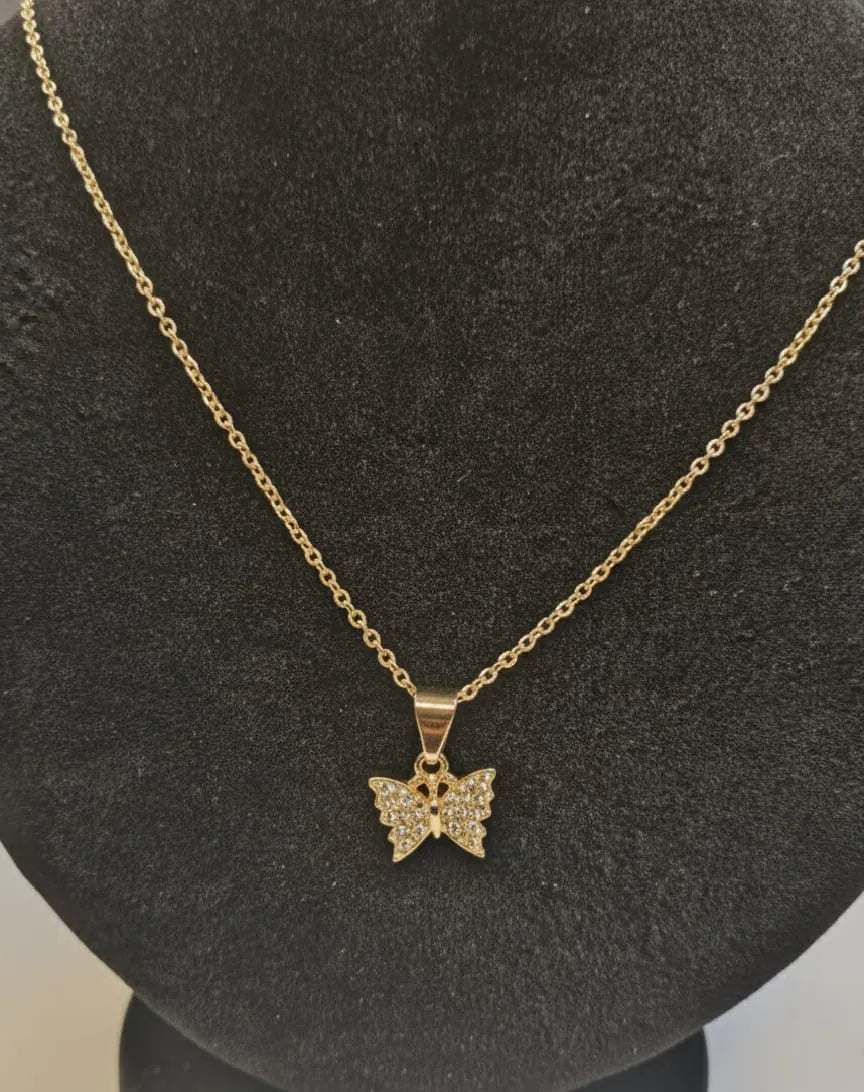 Woman with dark hair and a light-colored top, wearing a butterfly necklace, outdoors.