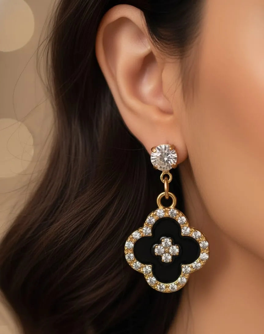 Close-up of a woman wearing a black clover-shaped earring with gold and clear stones.