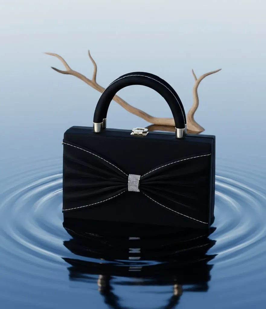 Black handbag with a decorative bow on a reflective water surface