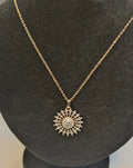 Gold necklace with a sunflower-shaped pendant on a black stand.